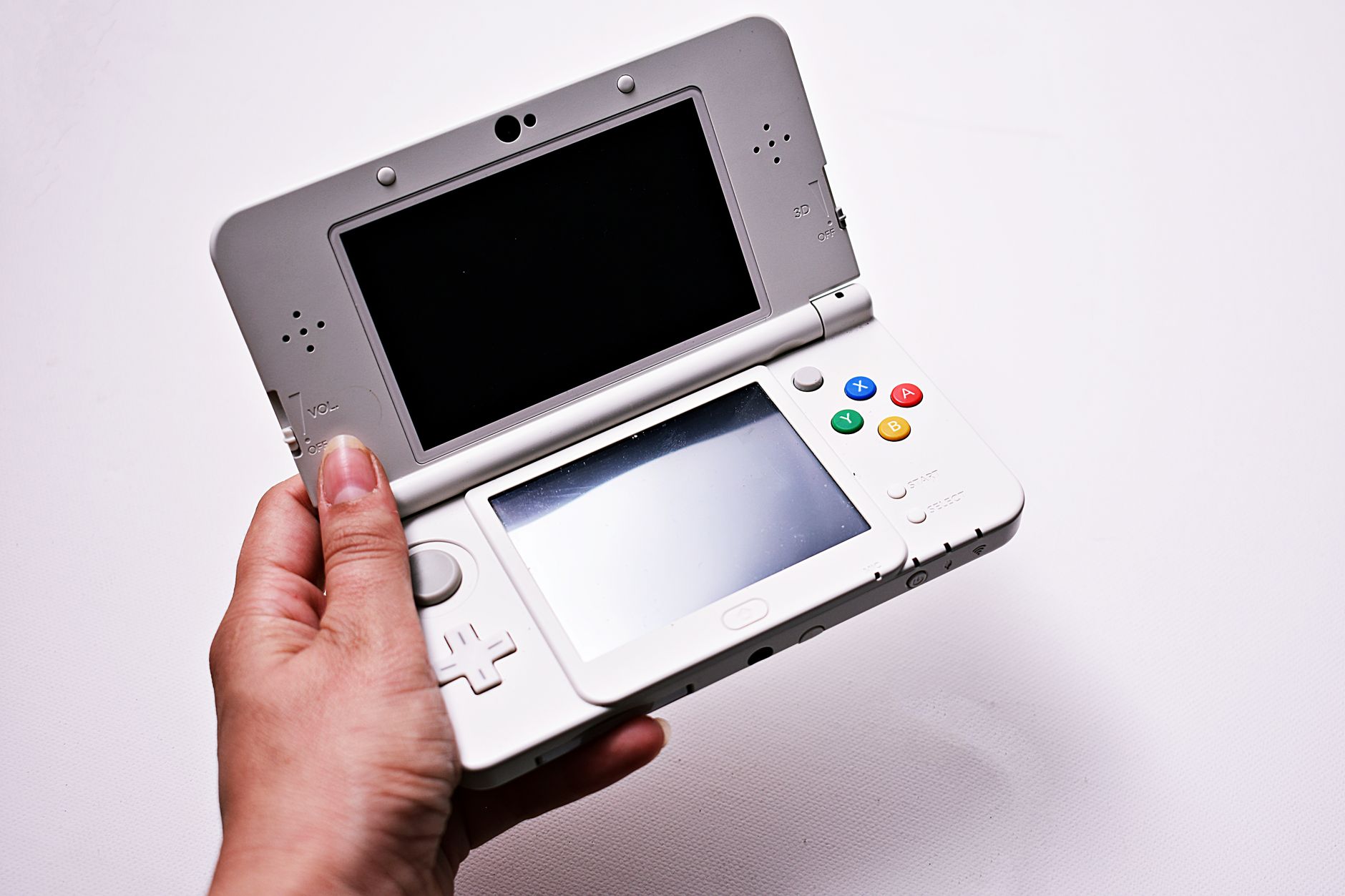 Gros plan d'une main tenant une console de jeu portable ouverte, dotée de deux écrans.