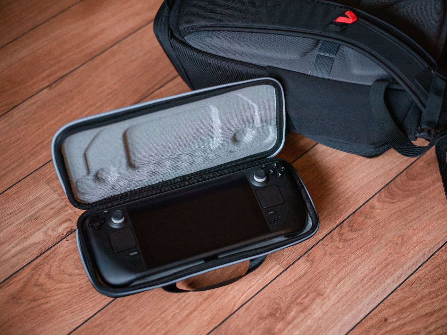 Une console de jeu portable dans un étui de protection sur un sol en bois avec un sac à dos.