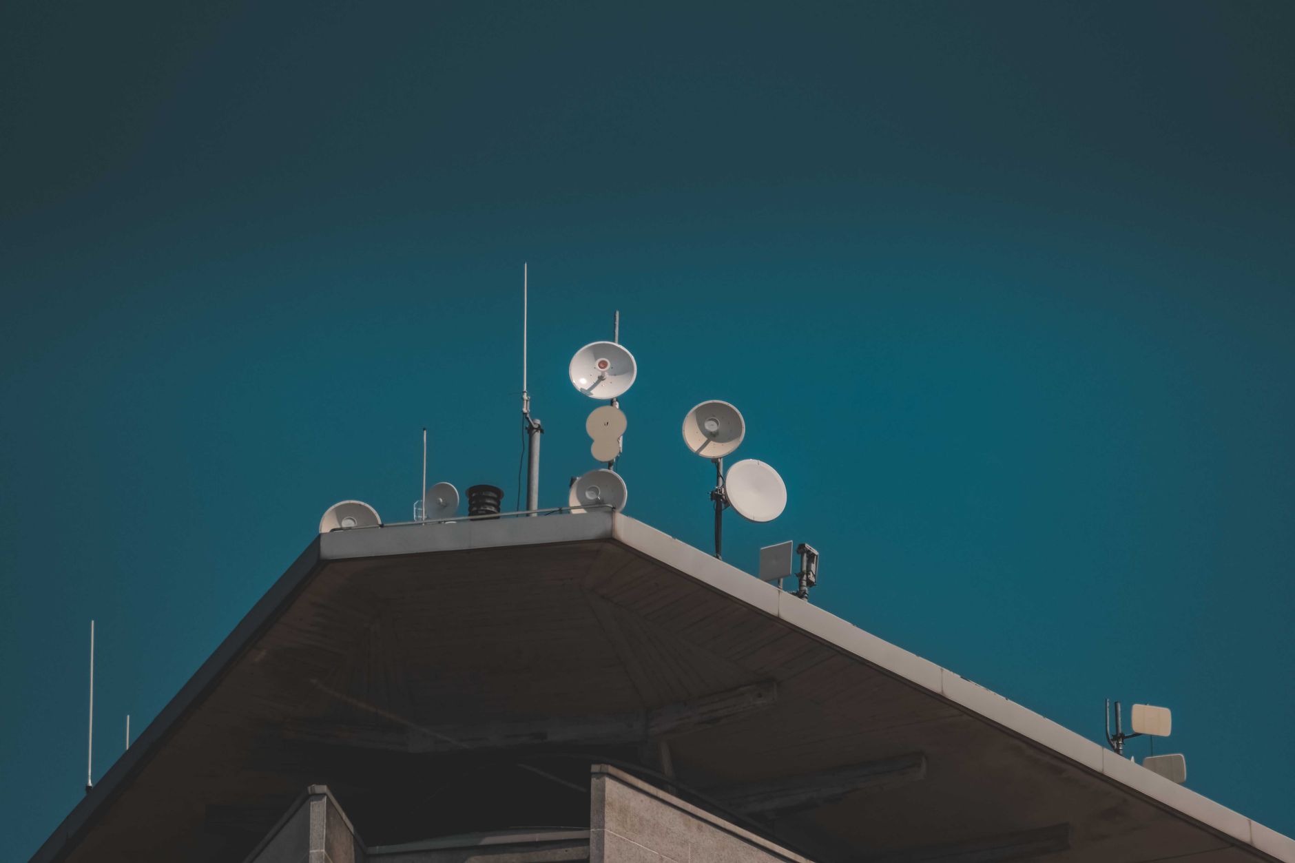 Vue en contre-plongée de plats et d'antennes de communication sur un bâtiment sur fond de ciel bleu clair.