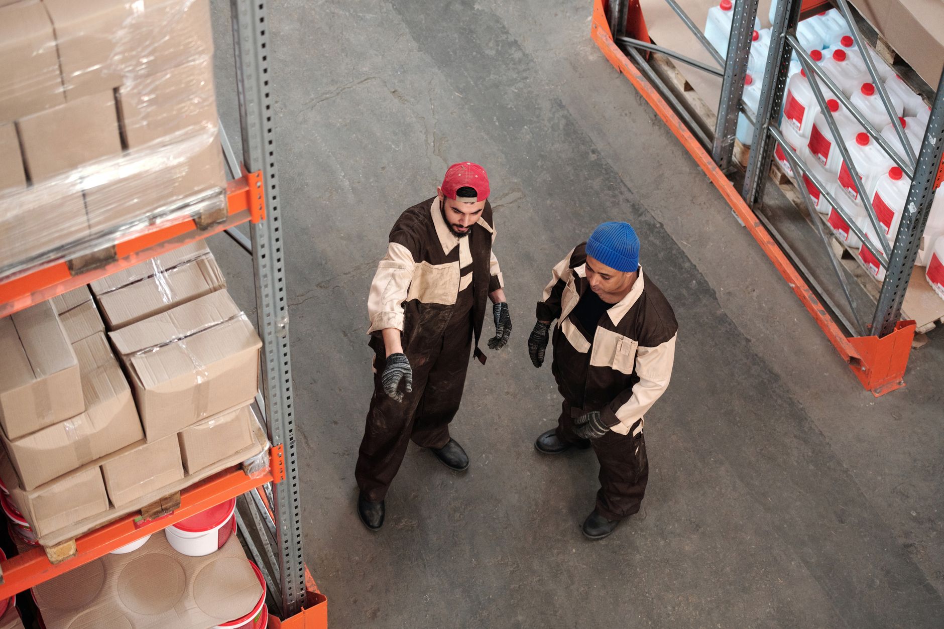 Deux hommes adultes dans un entrepôt communiquant sur la logistique de stockage, entourés d'étagères de colis.
