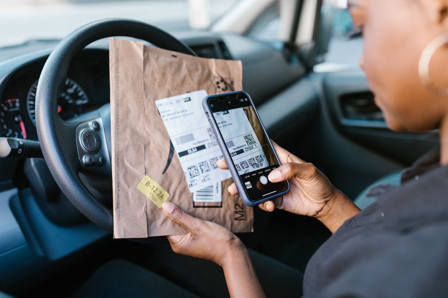 Gros plan d'un coursier dans une voiture scannant une étiquette de colis avec un smartphone pour un service de livraison.