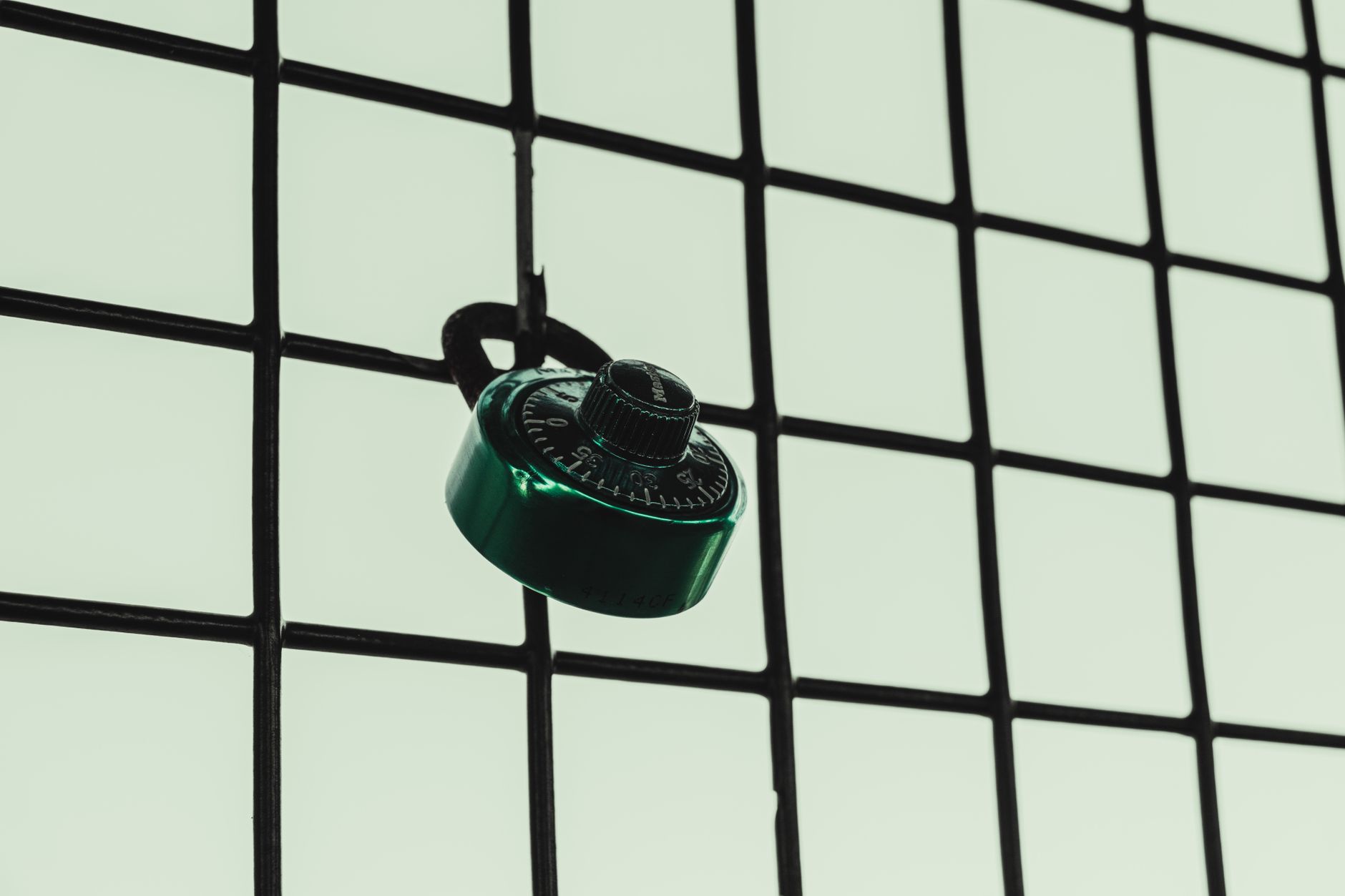 Cadenas à combinaison vert accroché à une grille métallique noire sur fond clair