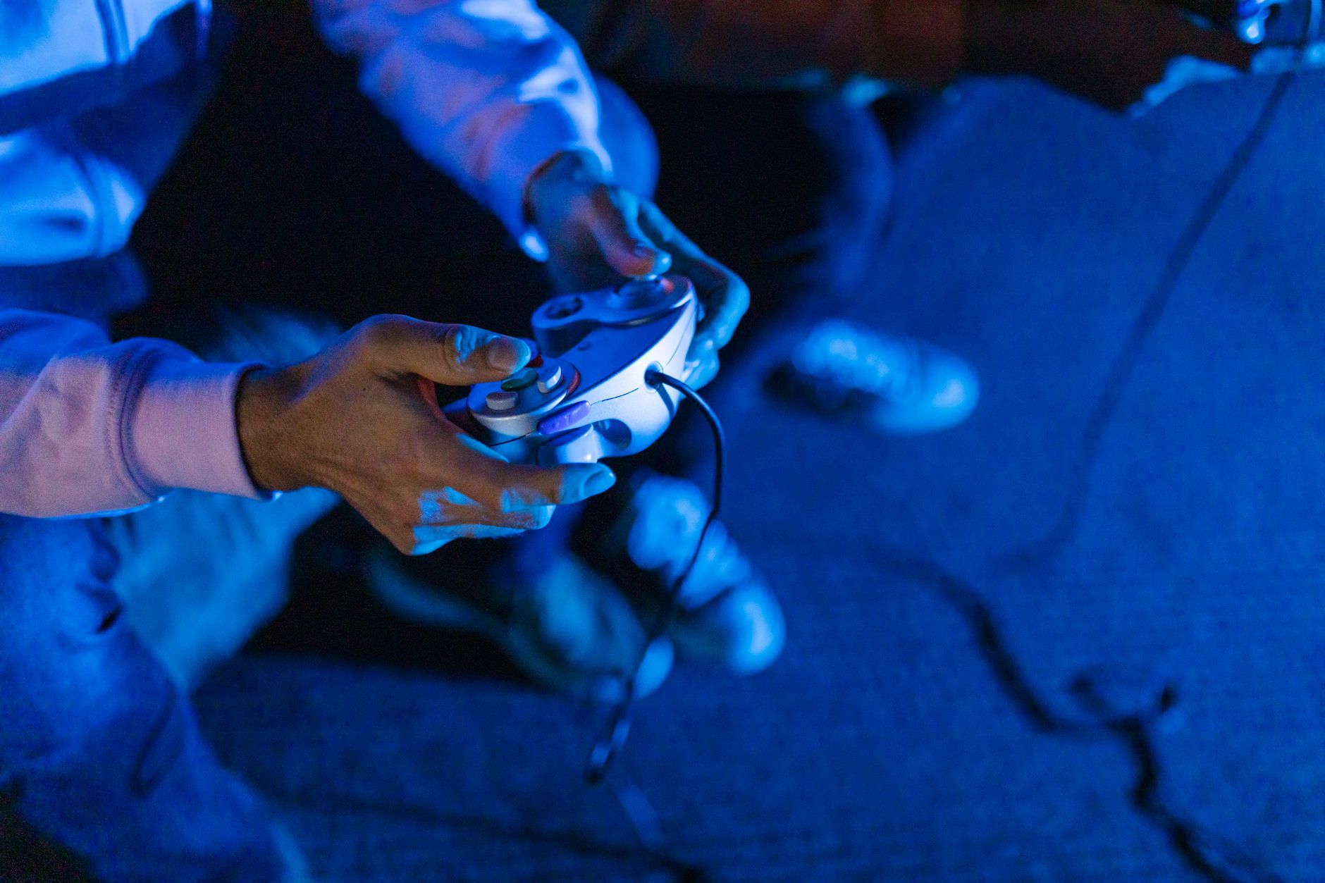 Gros plan sur les mains d’un joueur tenant une manette de jeu vidéo sous un éclairage bleu.
